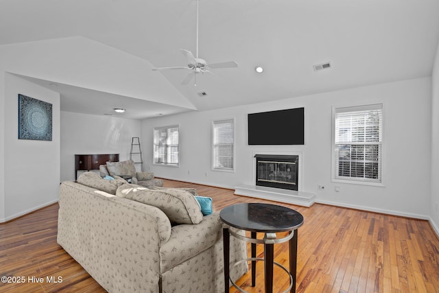 living area with a glass covered fireplace, visible vents, vaulted ceiling, and wood finished floors