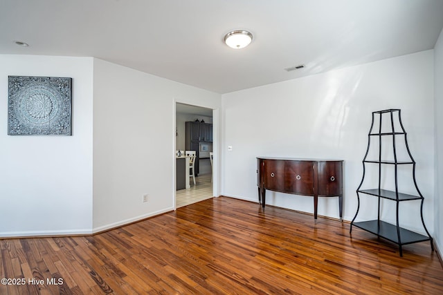 empty room with wood-type flooring, visible vents, and baseboards