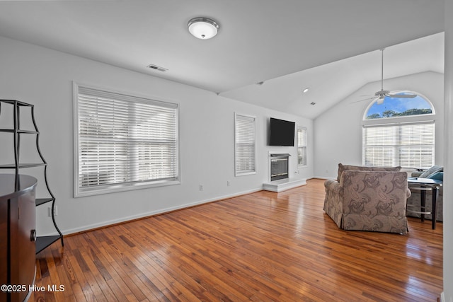 living room featuring lofted ceiling, hardwood / wood-style flooring, visible vents, baseboards, and a glass covered fireplace