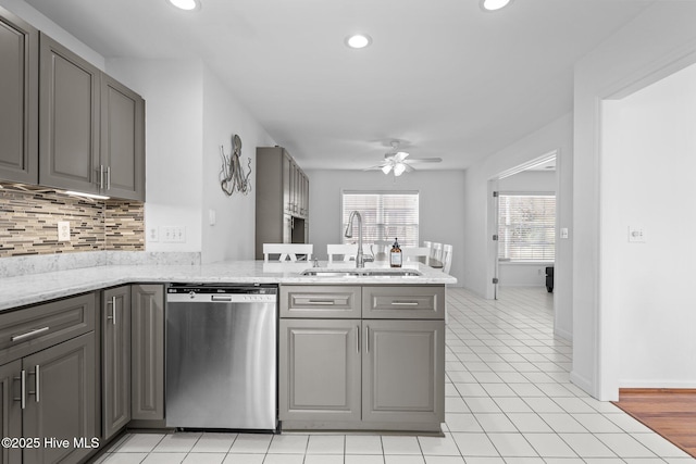 kitchen with gray cabinetry, a peninsula, a sink, stainless steel dishwasher, and backsplash