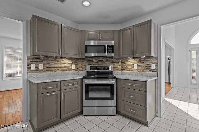 kitchen with appliances with stainless steel finishes, tasteful backsplash, gray cabinetry, and light tile patterned floors