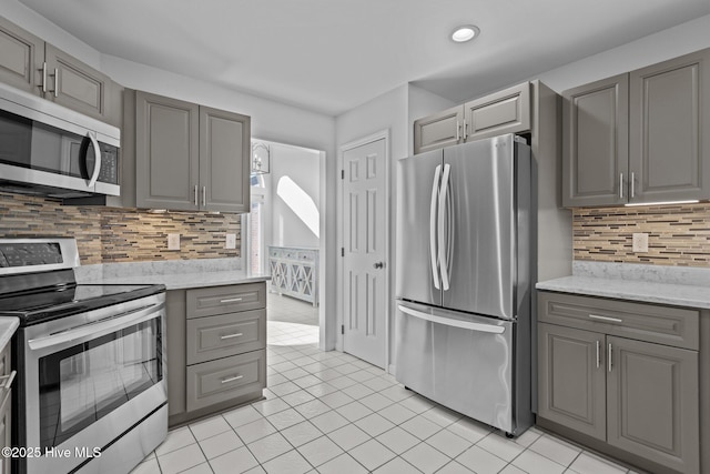 kitchen featuring stainless steel appliances, gray cabinets, light tile patterned flooring, and backsplash