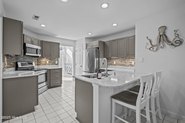 kitchen featuring gray cabinetry, a peninsula, a sink, visible vents, and appliances with stainless steel finishes