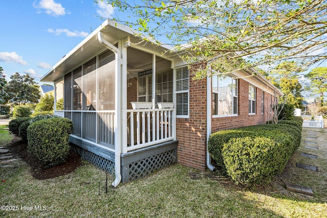 view of property exterior with a sunroom, brick siding, and a lawn