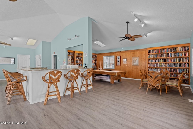 interior space featuring light wood finished floors, vaulted ceiling, a textured ceiling, wooden walls, and ceiling fan