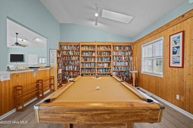 game room featuring lofted ceiling, rail lighting, a ceiling fan, wooden walls, and wood finished floors