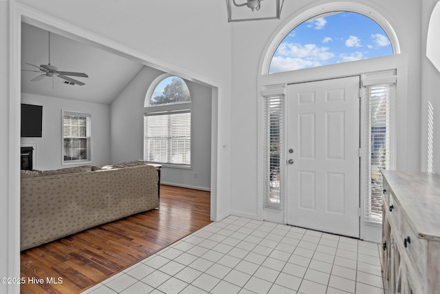 entrance foyer with lofted ceiling, a glass covered fireplace, ceiling fan, and light tile patterned floors