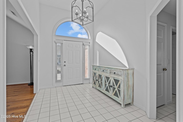 foyer featuring a towering ceiling, light tile patterned floors, baseboards, and a chandelier