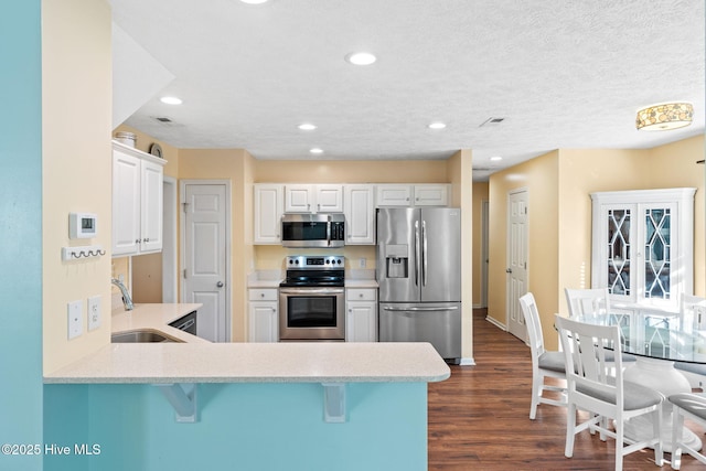 kitchen with a breakfast bar area, a peninsula, dark wood-style flooring, a sink, and appliances with stainless steel finishes