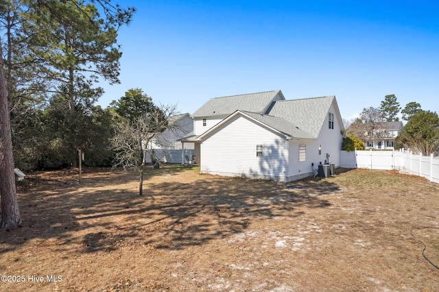 exterior space with central AC, roof with shingles, and fence