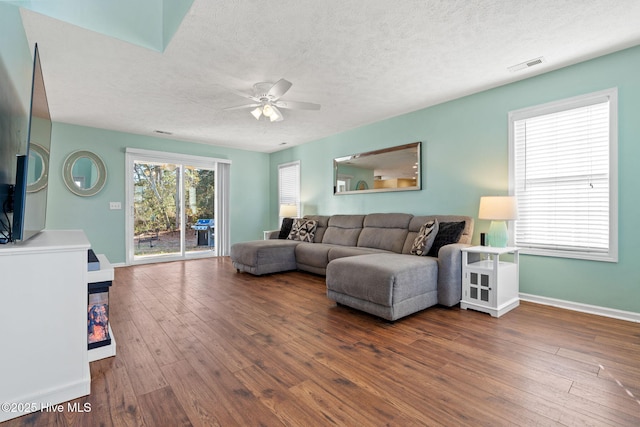 living room featuring a textured ceiling, ceiling fan, visible vents, baseboards, and wood-type flooring