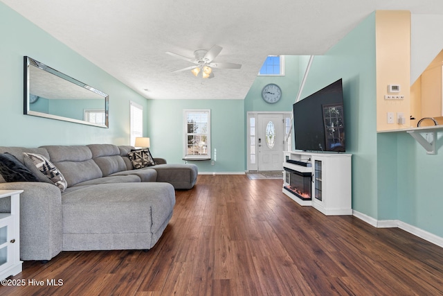 living room featuring a ceiling fan, a glass covered fireplace, a textured ceiling, wood finished floors, and baseboards