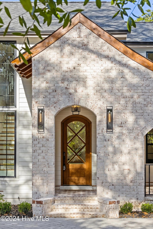 property entrance featuring a shingled roof and brick siding