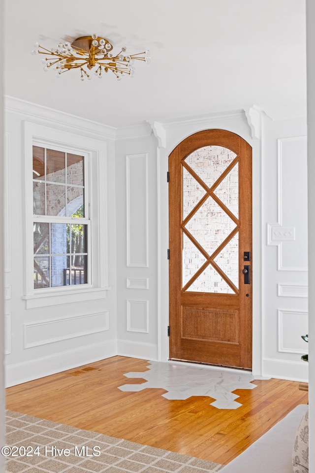 foyer featuring arched walkways, a decorative wall, wood finished floors, and crown molding