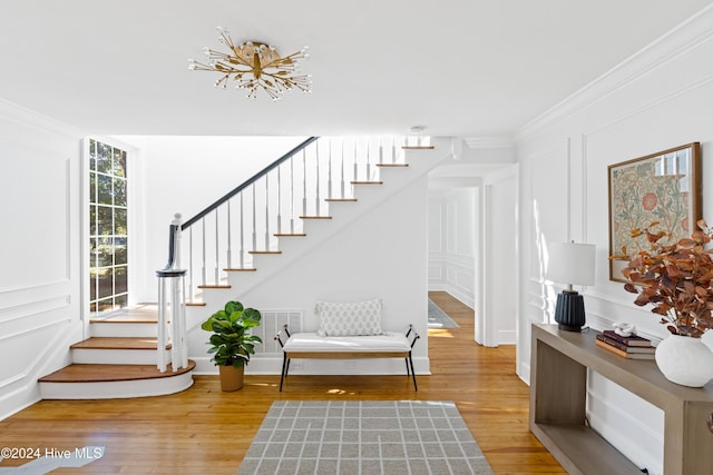 entrance foyer with stairs, ornamental molding, wood finished floors, and a decorative wall