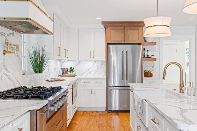 kitchen with stainless steel appliances, a sink, exhaust hood, light wood-type flooring, and tasteful backsplash