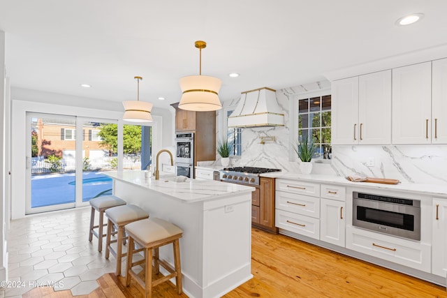 kitchen featuring light stone counters, a kitchen breakfast bar, custom exhaust hood, stainless steel appliances, and backsplash