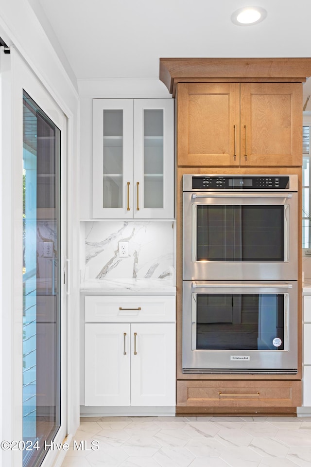 kitchen with double oven, white cabinets, marble finish floor, decorative backsplash, and glass insert cabinets