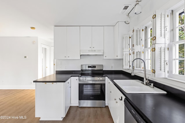 kitchen featuring stainless steel appliances, dark countertops, a sink, a peninsula, and under cabinet range hood