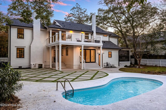 back of house at dusk featuring a balcony, fence, a sunroom, a fenced in pool, and a patio area