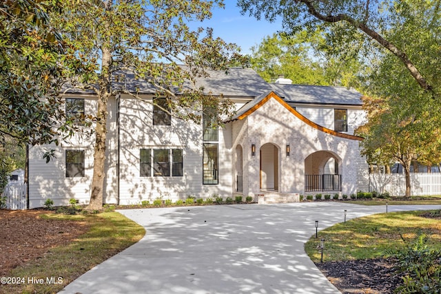 french provincial home featuring concrete driveway, brick siding, and a chimney