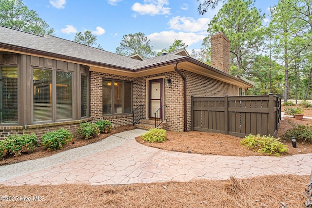 entrance to property featuring a shingled roof, brick siding, and a chimney