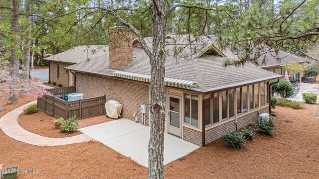 back of property with brick siding, roof with shingles, concrete driveway, a sunroom, and a patio area