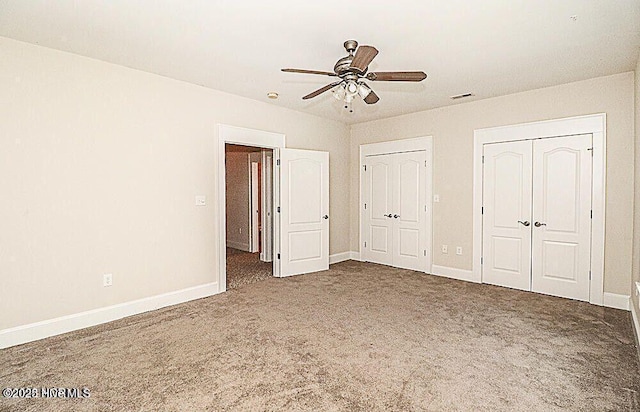 unfurnished bedroom with visible vents, carpet flooring, two closets, and baseboards