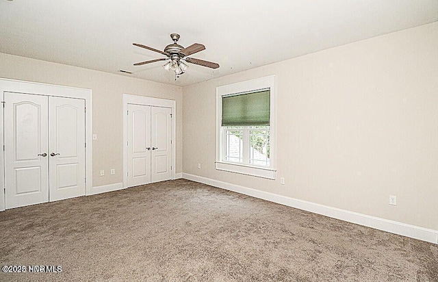 unfurnished bedroom with carpet floors, multiple closets, a ceiling fan, and baseboards