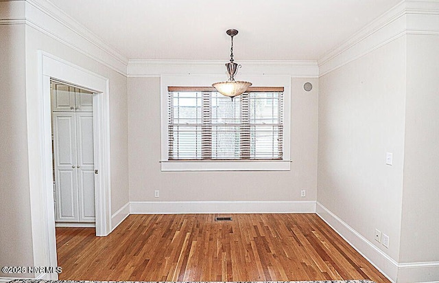 unfurnished dining area featuring baseboards, wood finished floors, visible vents, and crown molding