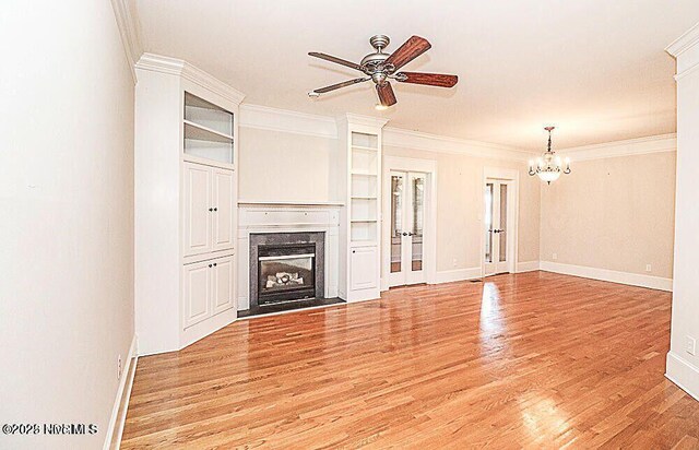 unfurnished living room featuring ceiling fan with notable chandelier, a high end fireplace, baseboards, light wood-type flooring, and crown molding