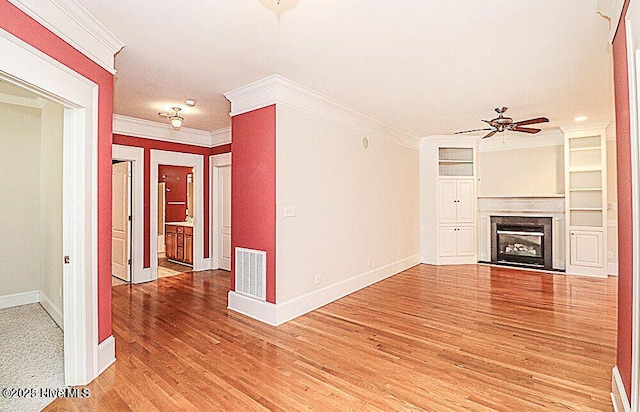 unfurnished living room with crown molding, a fireplace, visible vents, light wood-style flooring, and a ceiling fan