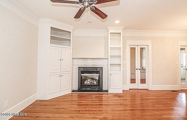 unfurnished living room with french doors, wood finished floors, a glass covered fireplace, and crown molding