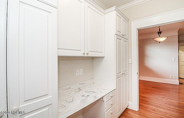 kitchen featuring light wood-style floors, white cabinets, crown molding, and built in study area