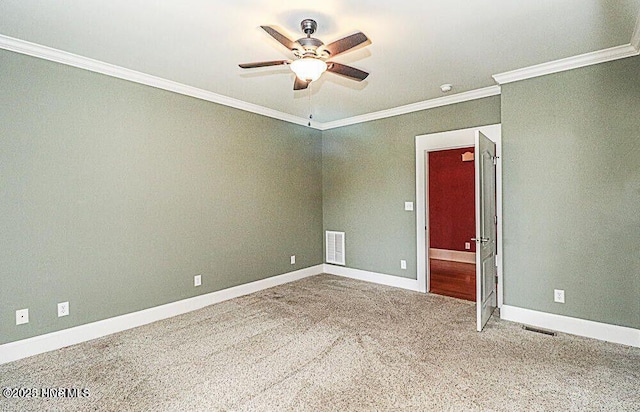 carpeted empty room with ornamental molding, a ceiling fan, visible vents, and baseboards