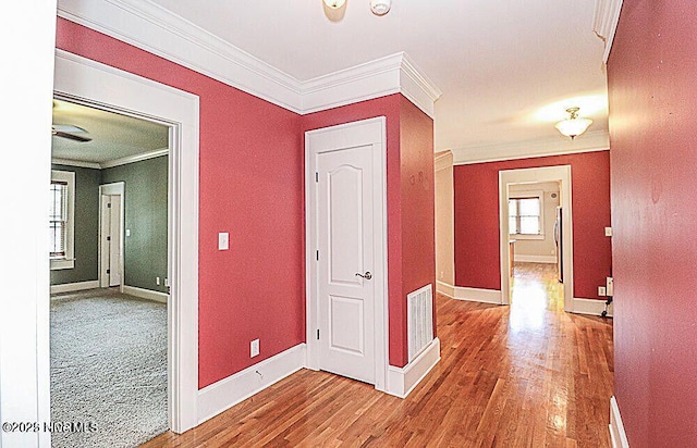 hallway with baseboards, visible vents, ornamental molding, and wood finished floors