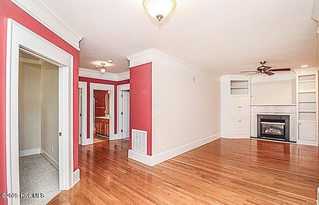 unfurnished living room featuring visible vents, a ceiling fan, ornamental molding, wood finished floors, and a fireplace