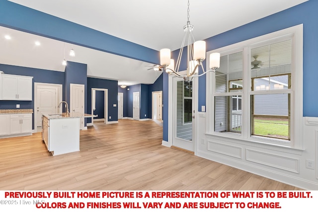 unfurnished dining area with a notable chandelier, light wood-style flooring, a sink, a decorative wall, and vaulted ceiling with beams