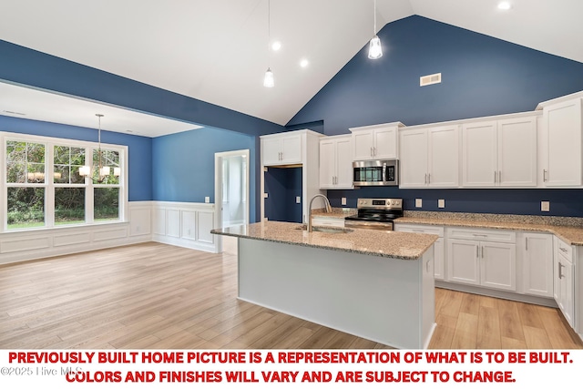 kitchen with a sink, stainless steel appliances, a wainscoted wall, and white cabinetry