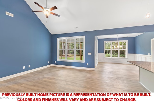 unfurnished living room with visible vents, ceiling fan with notable chandelier, light wood-style flooring, and a wainscoted wall