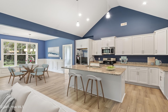 kitchen featuring a sink, white cabinetry, stainless steel appliances, light wood-style floors, and wainscoting