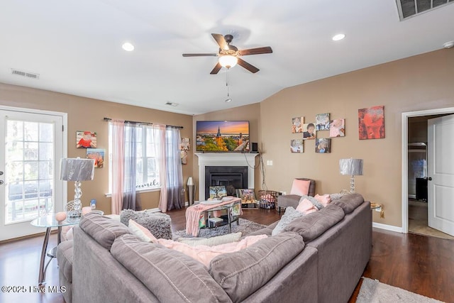 living room featuring lofted ceiling, dark wood finished floors, a glass covered fireplace, and visible vents