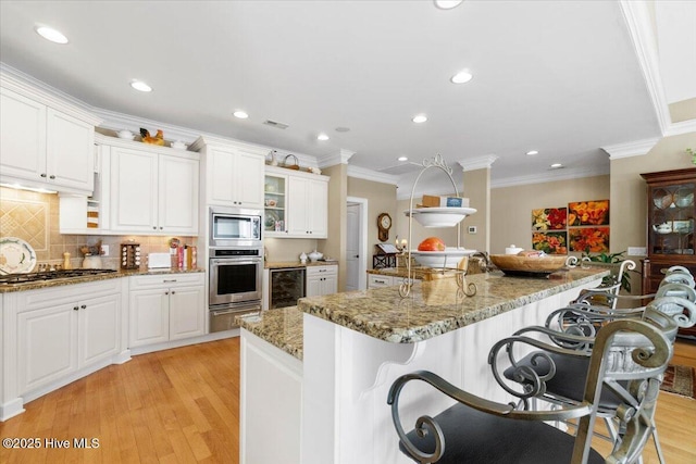 kitchen featuring light wood finished floors, stainless steel appliances, wine cooler, ornamental molding, and a kitchen bar