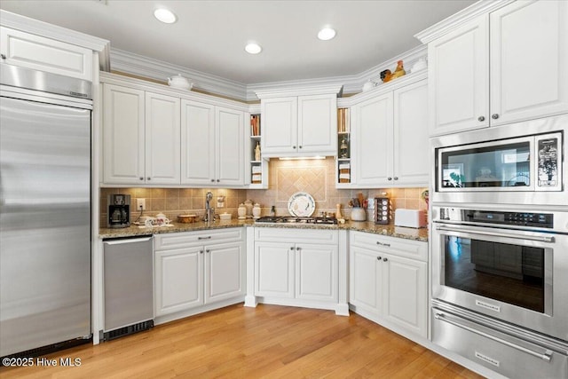 kitchen with white cabinets, light wood finished floors, light stone counters, a warming drawer, and built in appliances