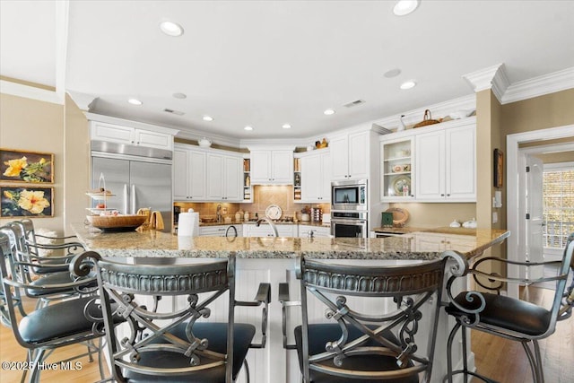 kitchen with crown molding, a sink, light wood-type flooring, built in appliances, and visible vents