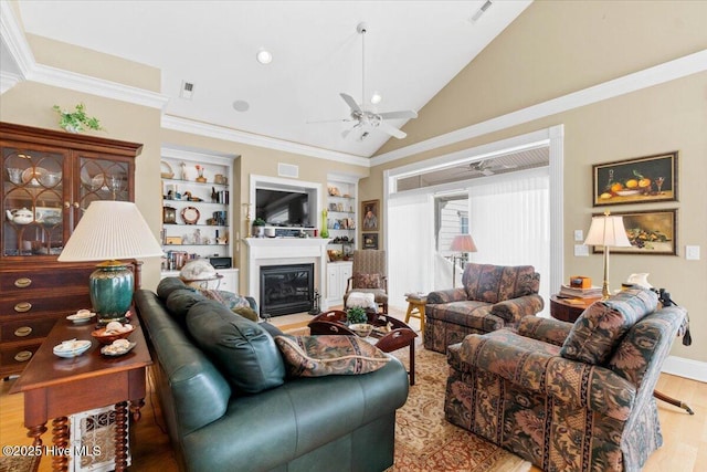 living area featuring wood finished floors, visible vents, a glass covered fireplace, built in features, and ceiling fan