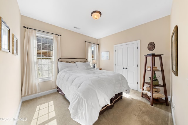 bedroom with baseboards, visible vents, a closet, and light colored carpet