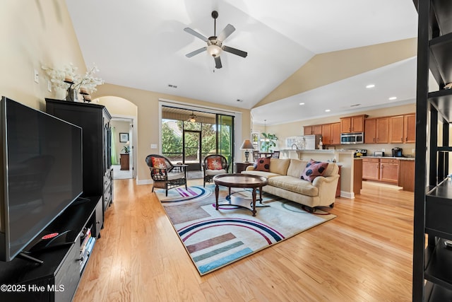 living room featuring light wood finished floors, arched walkways, baseboards, a ceiling fan, and high vaulted ceiling