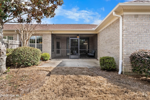 view of exterior entry featuring a patio, brick siding, and fence