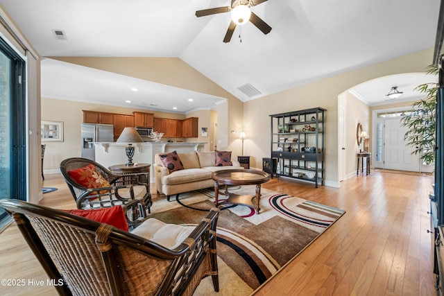 living room featuring light wood-type flooring, arched walkways, visible vents, and ornamental molding